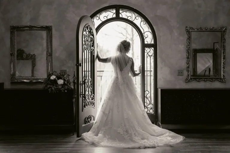 Black and white photo of gorgeous bride showcasing the back of her beautiful wedding dress in front of a large metal door