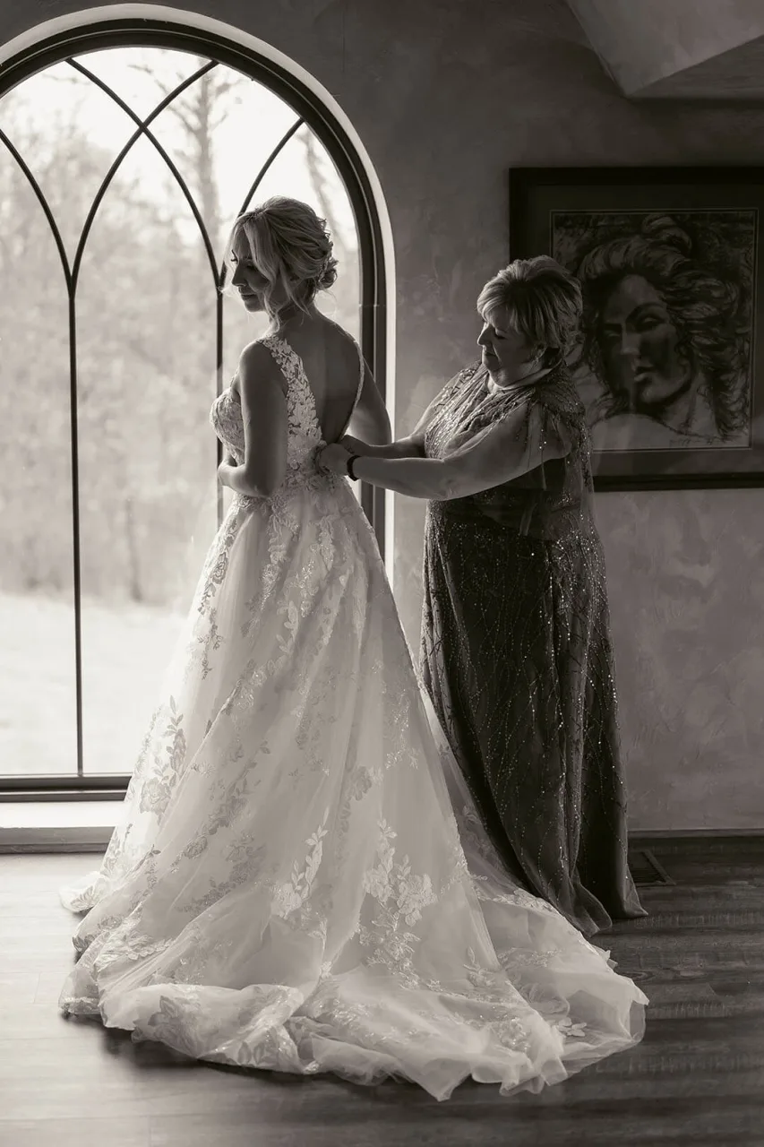 Black and white photo of bride and her mother putting on her wedding dress