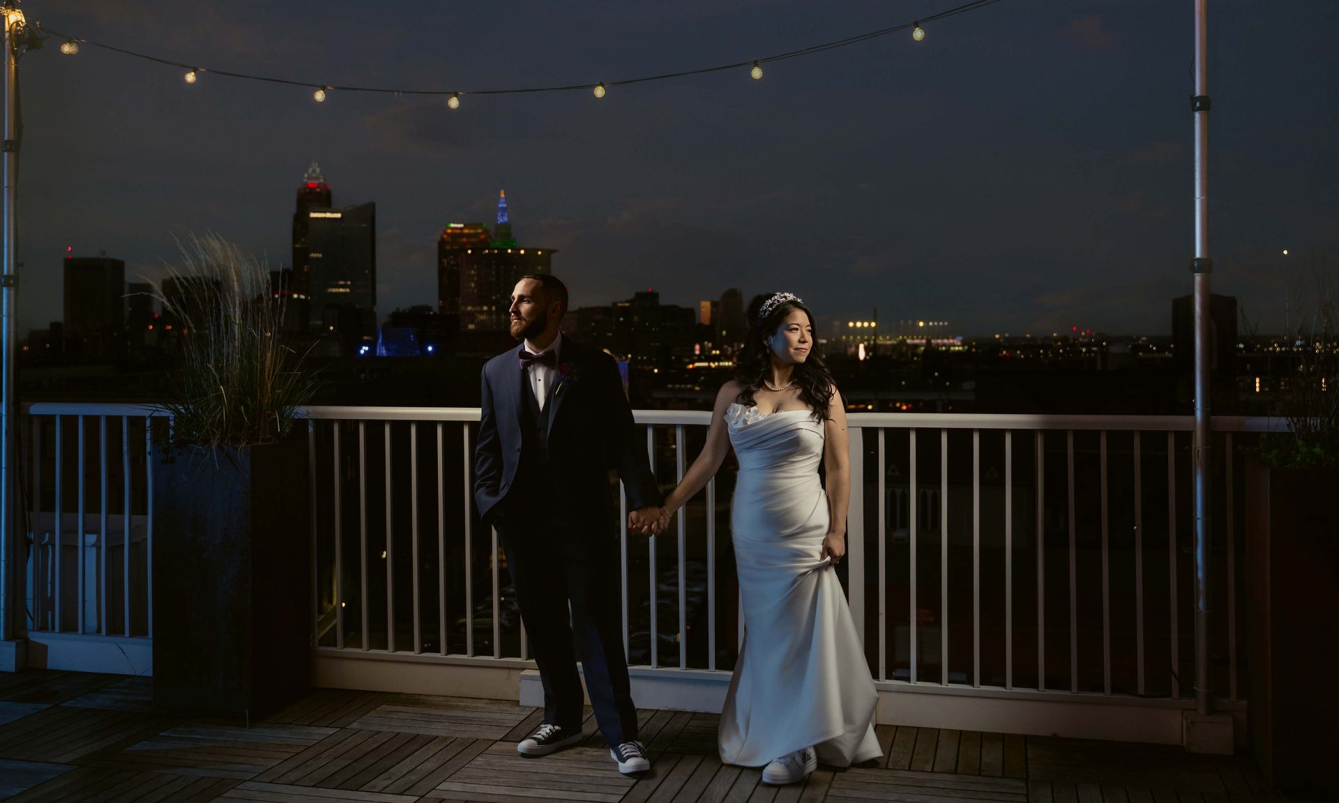 Wedding couple standing side by side on the rooftop of Lantern Room by Penthouse Events, dramatically lit with the Cleveland, Ohio skyline in the background - Wedding Photography by Kropp Photography