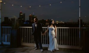 Wedding couple standing side by side on the rooftop of Lantern Room by Penthouse Events, dramatically lit with the Cleveland, Ohio skyline in the background - Wedding Photography by Kropp Photography